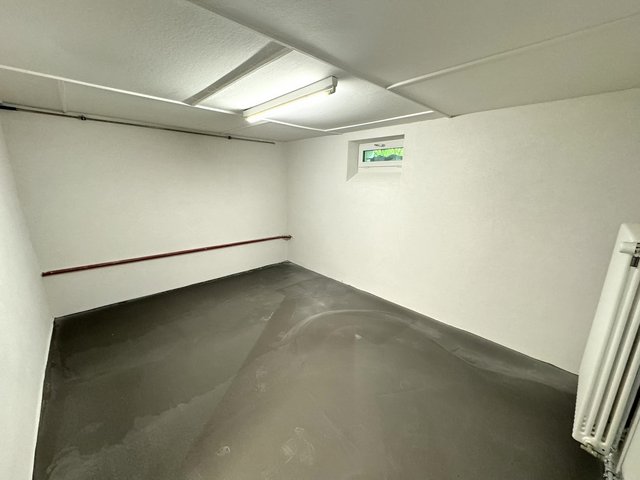 Leerer Kellerraum mit weißer Decke, kleinem Fenster und grauem Bodenbelag