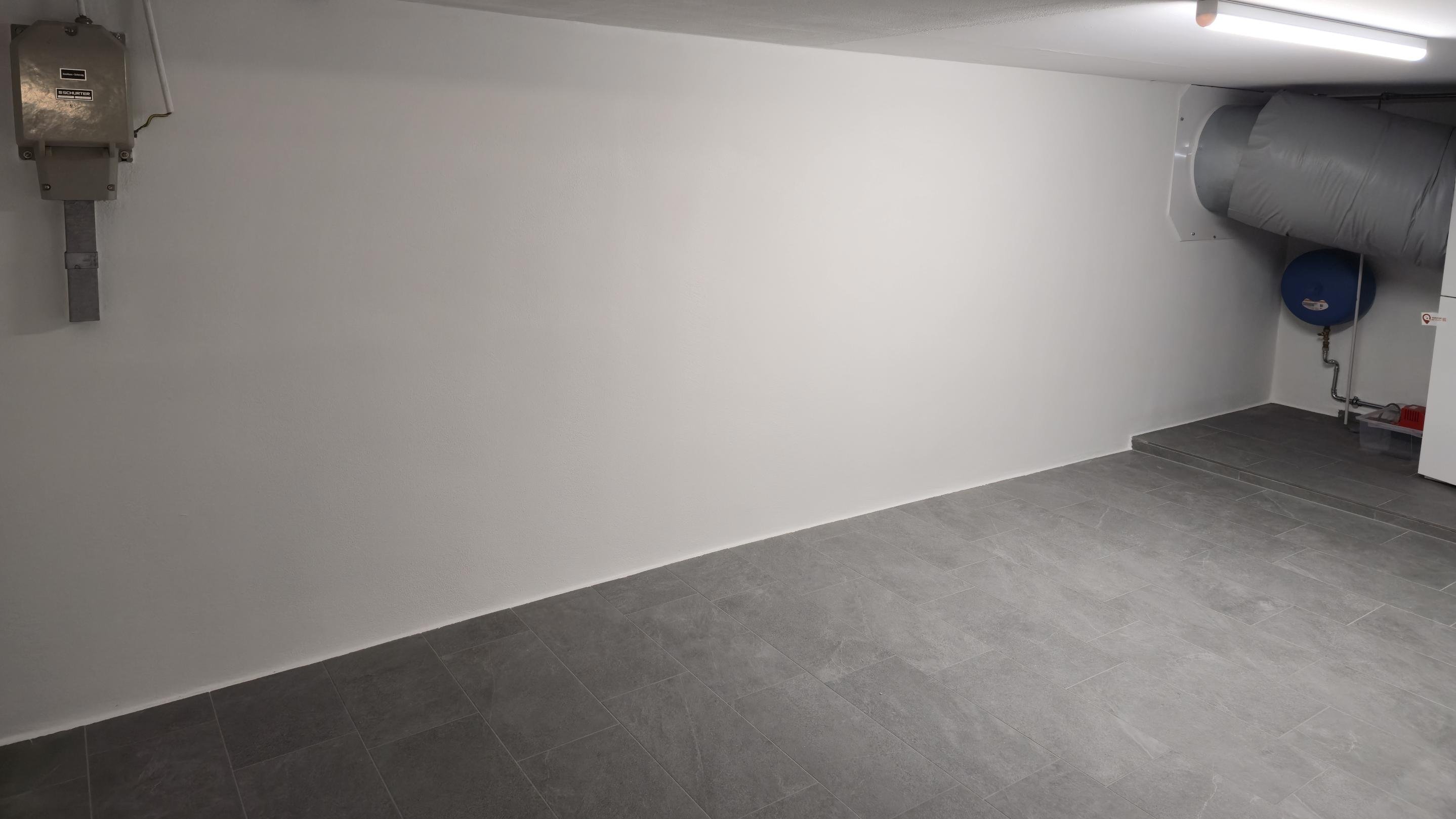 Heller Kellerraum mit weißer Wand, Fliesenboden, Lüftungsrohr und Leuchtstofflampe