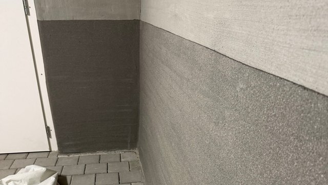Graue Sockelbeschichtung an Kellerwand über Pflasterboden, Ecke neben weißer Tür