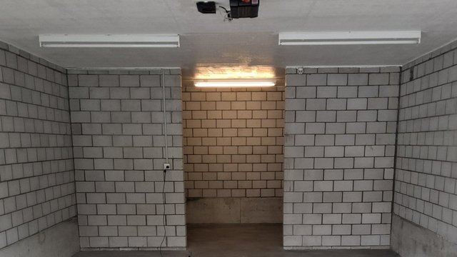 Leerer Kellerraum mit grauen Mauersteinwänden, Betonboden und Leuchtstoffröhren.