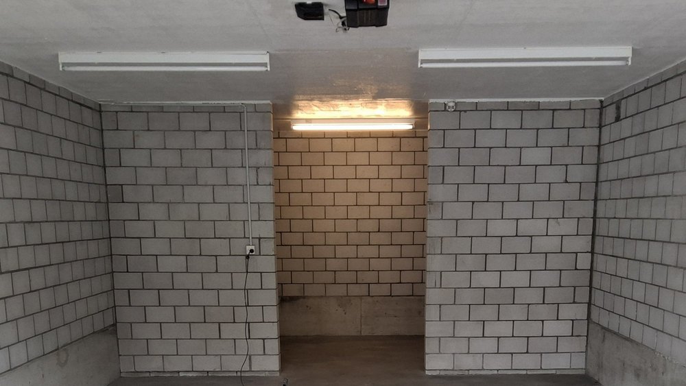 Leerer Kellerraum mit grauen Mauersteinwänden, Betonboden und Leuchtstoffröhren.
