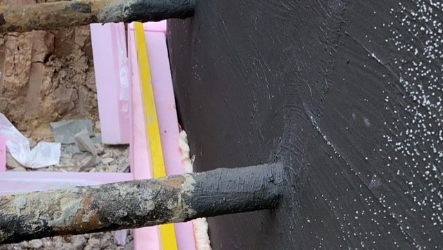 Schwarze Masse auf Kellerwand, Nahaufnahme mit Durchführungsrohren