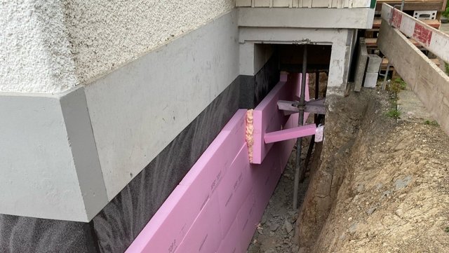 Rosa Dämmplatten an freigelegter Kellerwand unter Gebäude montiert