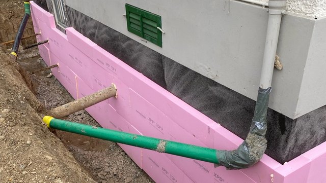 Rosa Dämmplatten an freigelegter Gebäudewand mit Rohrdurchführungen im Erdreich