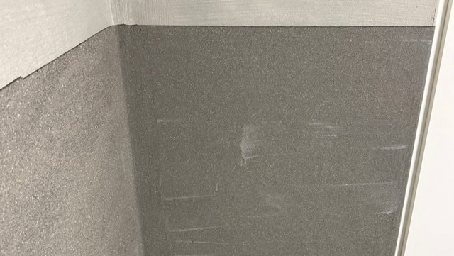Dunkelgraue Masse auf Wandfläche mit Ecke, rechts weiße Kante