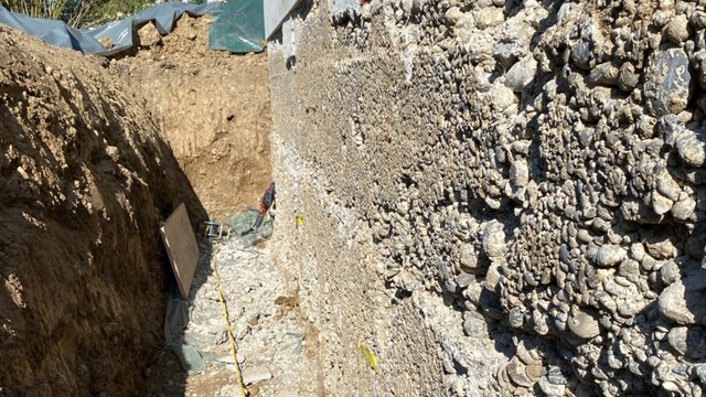 Freigelegte Betonwand mit grober Gesteinskörnung im Erdgraben