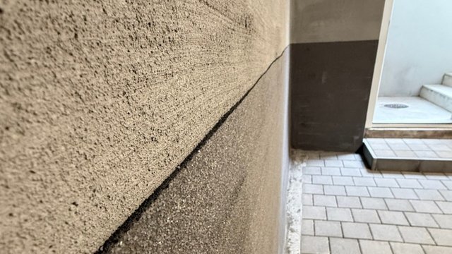 Schwarze Abdichtungsbahn an rauer Kellerwand, Nahaufnahme mit Fliesenboden