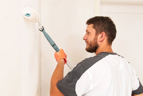 Worker applies white paint to wall.