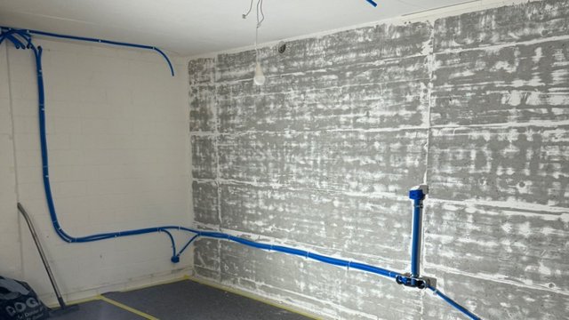 Freigelegte Betonwand mit blauen Leitungen in leerem Raum