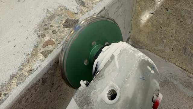 Trennschleifer mit grüner Scheibe schneidet Beton an einer Ecke.