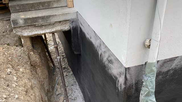 Schwarze Masse an freigelegtem Gebäudesockel im Erdgraben
