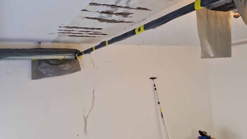 Mitarbeiter trägt mit langer Stange graue Masse auf Decke auf.