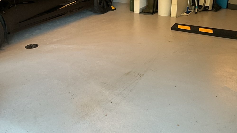 Grauer Garagenboden mit Abfluss, Reifenspuren und geparktem Auto