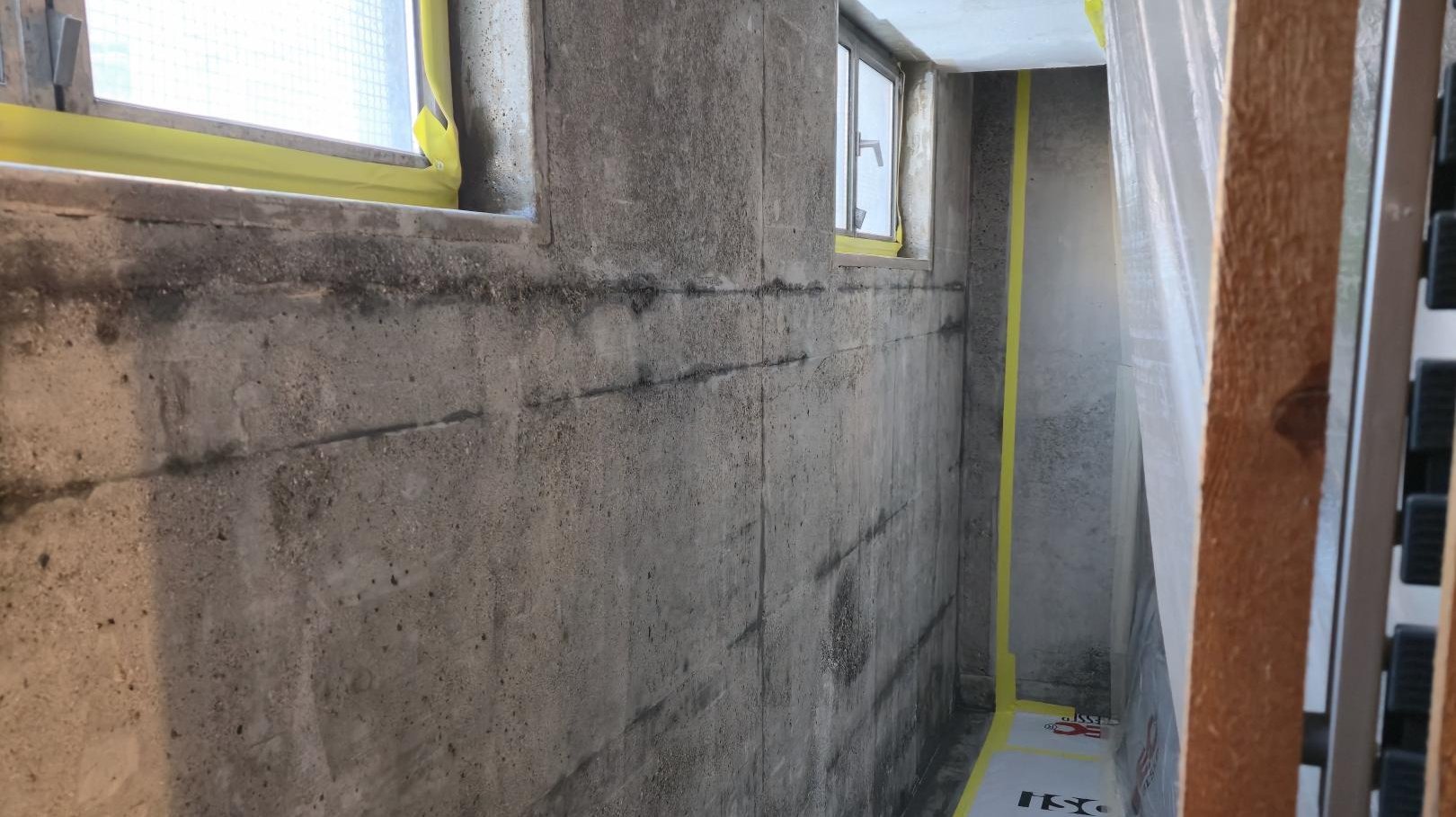 Abgeklebter Kellerraum mit Betonwand, Fenstern und Schutzfolie am Boden