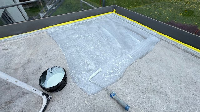 Farbrolle trägt helle Flüssigkeit auf Betonfläche eines Flachdachs auf