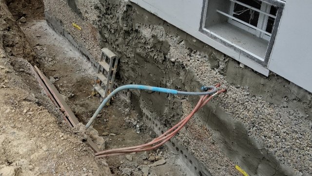 Freigelegte Hauswand mit Bohrlöchern, grauer Masse und Kabeln im Erdgraben