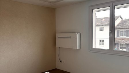 Wandgerät an heller Zimmerwand neben Fenster, leeres Zimmer mit Teppichboden
