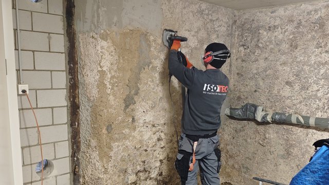 ISOTEC Mitarbeiter schleift raue Kellerwand mit elektrischem Schleifgerät ab