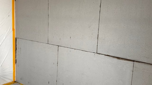 Hellgraue Plattenwand mit sichtbaren Fugen und Flecken, Nahaufnahme