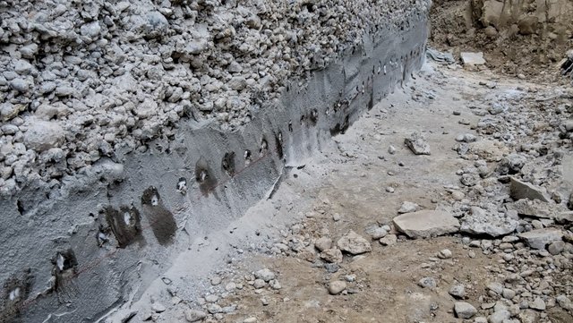 Bohrlöcher und graue Masse an Betonwand in Baugrube
