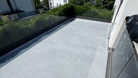 Hellgrauer Balkonboden mit Glasgeländer, Blick auf angrenzende Grünfläche