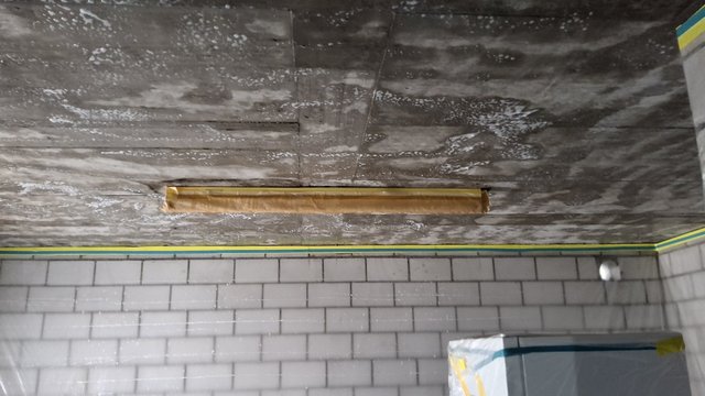 Graue Decke mit weißen Flecken über gefliester Kellerwand und Leuchte.