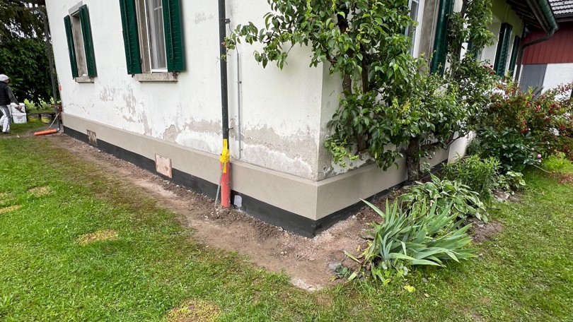 Freigelegter Sockelbereich am Haus mit schwarzer Abdichtung und Erdaushub