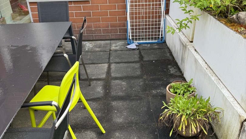 Verschmutzte Terrassenplatten neben Tisch und Stühlen, Pflanzkübel an Stufe.