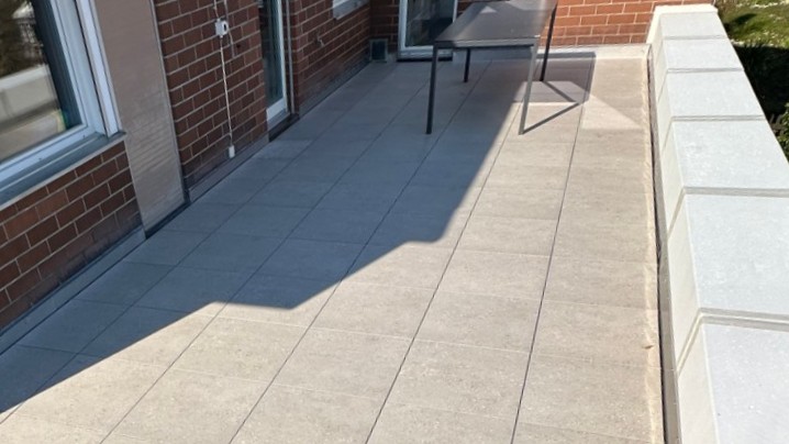 Balkon mit grauen Bodenplatten, Ziegelwand, Tisch und Brüstung im Sonnenlicht