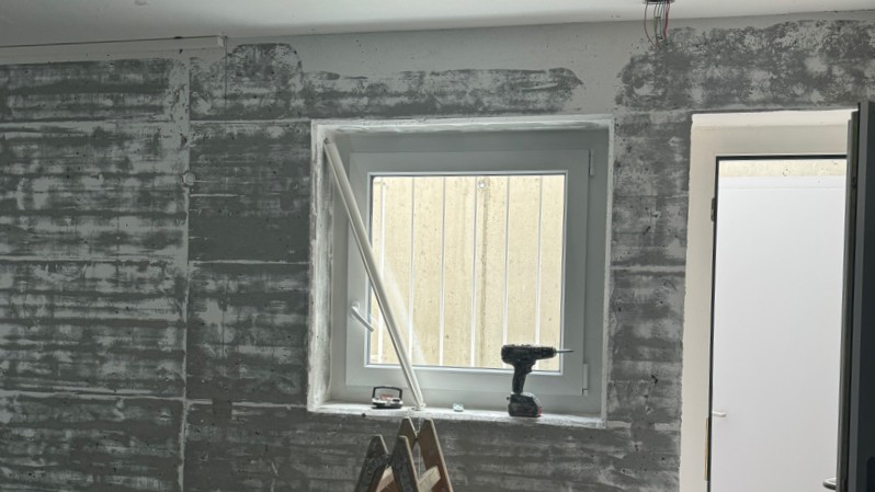 Freigelegte Wand mit Fensteröffnung und dunklen Rückständen im Raum
