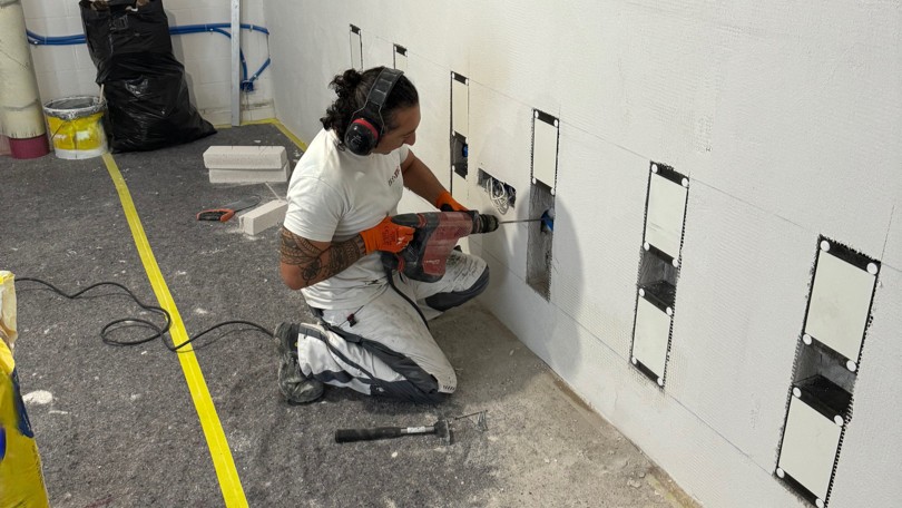 Arbeiter bohrt Löcher in helle Platte an Kellerwand