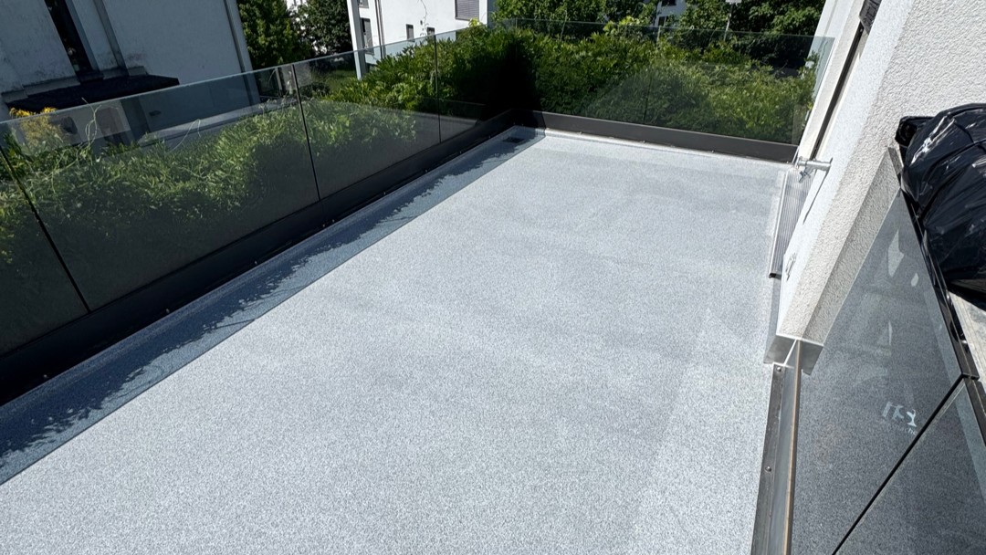 Hellgrauer Balkonboden mit Glasgeländer, Blick auf angrenzende Grünfläche