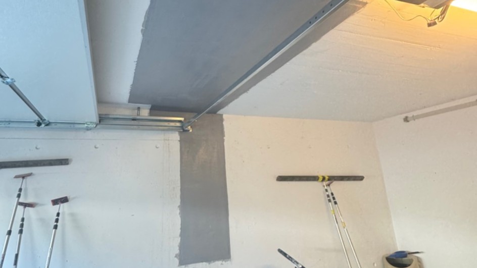 Garagendecke und Wand teilweise mit grauer Masse bearbeitet, Stielwerkzeuge hängen an der Wand