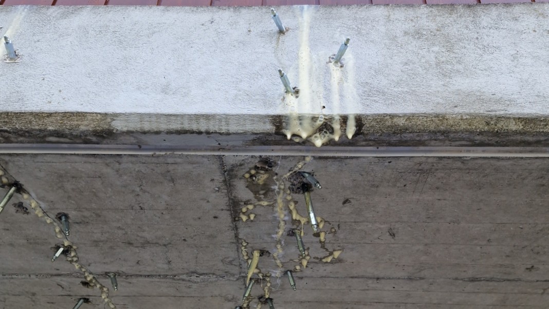 Metallische Gewindestangen ragen aus Betonwand, beige Masse tropft herab.