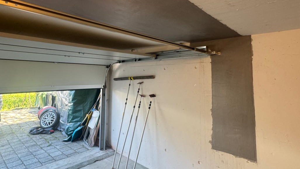 Garagenwand mit grauer Masse ausgebessert, Tor geöffnet, Geräte lehnen an Wand