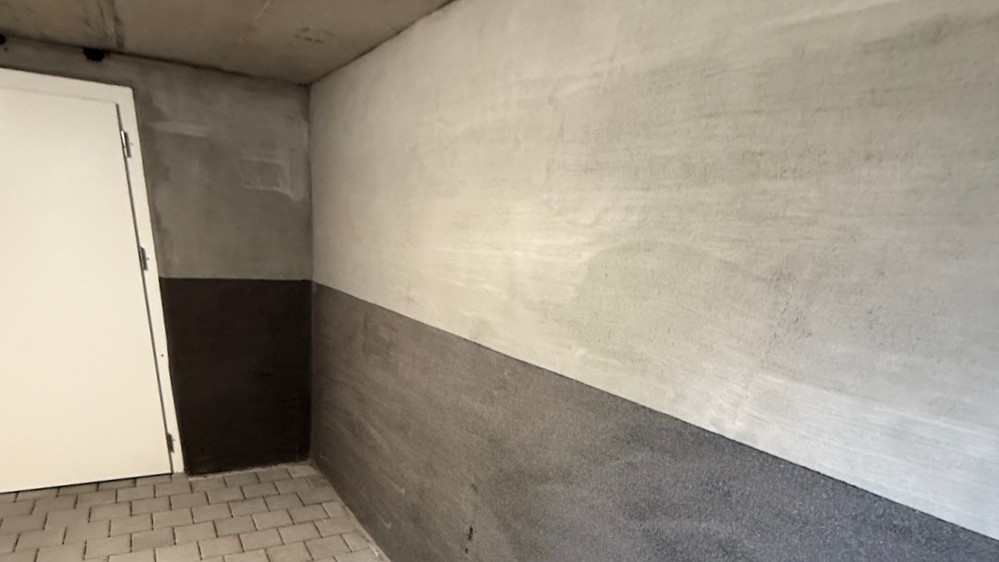 Weiß-grau gestrichene Kellerwand mit dunklem Sockelbereich und Tür, Fliesenboden