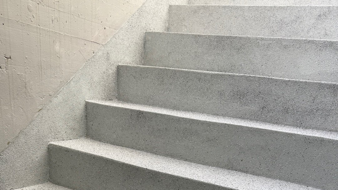 Graue Betontreppe im Treppenhaus, Detailansicht mit rauer Oberfläche.