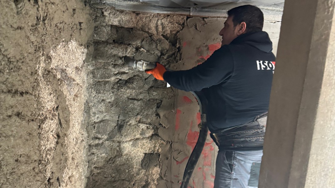 ISOTEC Mitarbeiter sprüht graue Masse auf grobe Wandoberfläche