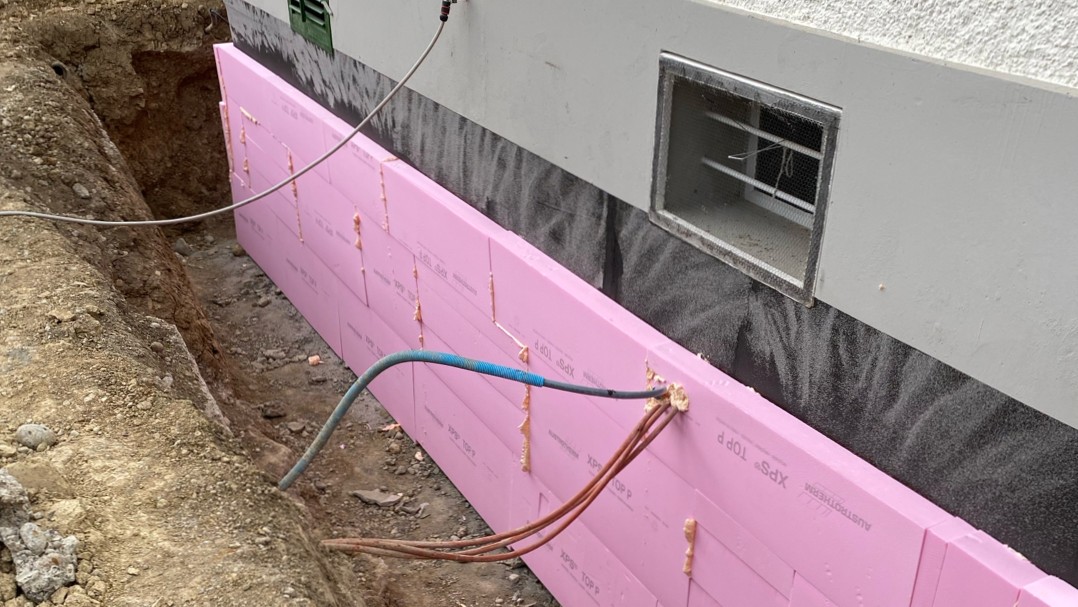 Rosa Dämmplatten an freigelegter Kellerwand mit schwarzer Masse und Kabeldurchführung