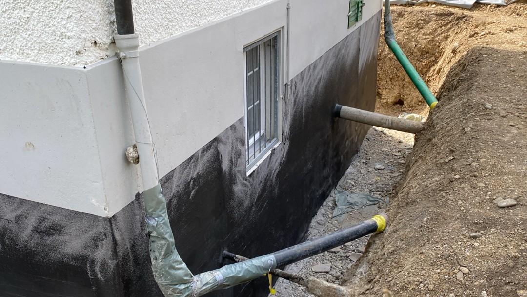 Freigelegte Kellerwand mit schwarzer Masse und Drainagerohren am Gebäude