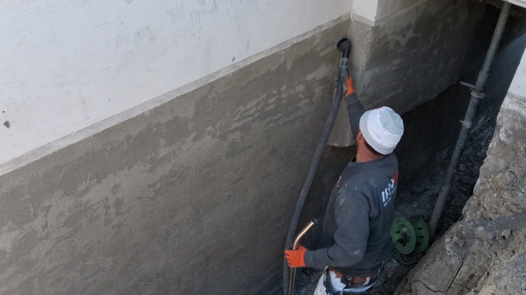 ISOTEC Mitarbeiter saugt Bohrmehl von freigelegter Hauswand im Graben ab