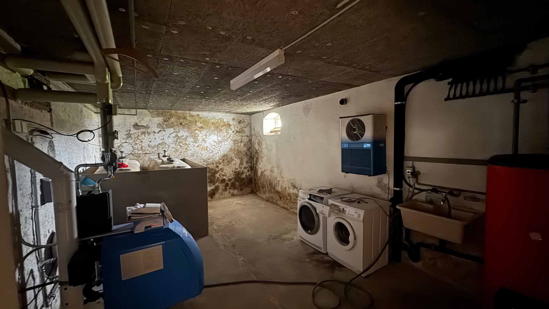 Feuchte Kellerwände mit dunklen Flecken in Waschraum mit Waschmaschinen