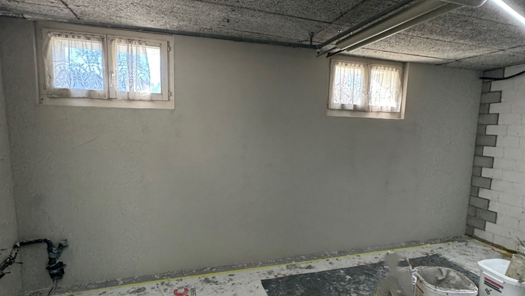 Leere Kellerwand mit zwei kleinen Fenstern, frisch verputzt