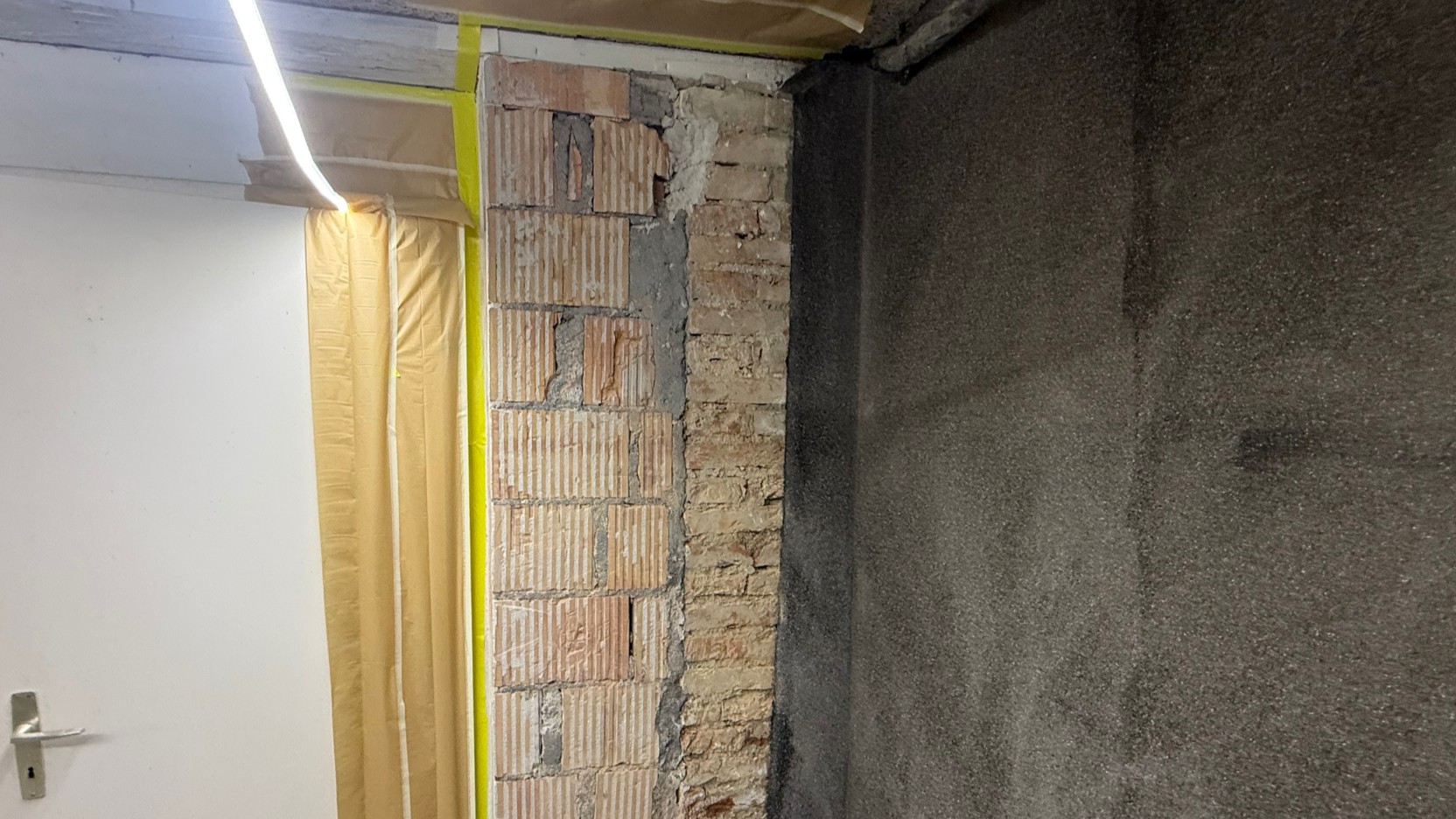 Freigelegte Ziegelwand neben schwarzer beschichteter Wand im Keller