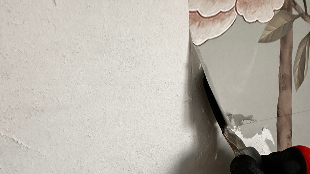 Spachtel löst helle Tapete von Wand mit Blumenmotiv, Nahaufnahme