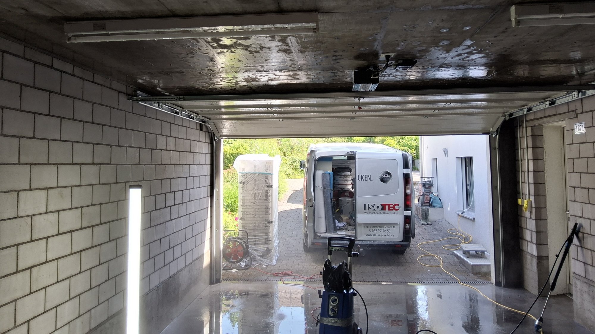 ISOTEC Transporter steht vor offener Garage, nasser Betonboden mit Kabeltrommel und Geräten.