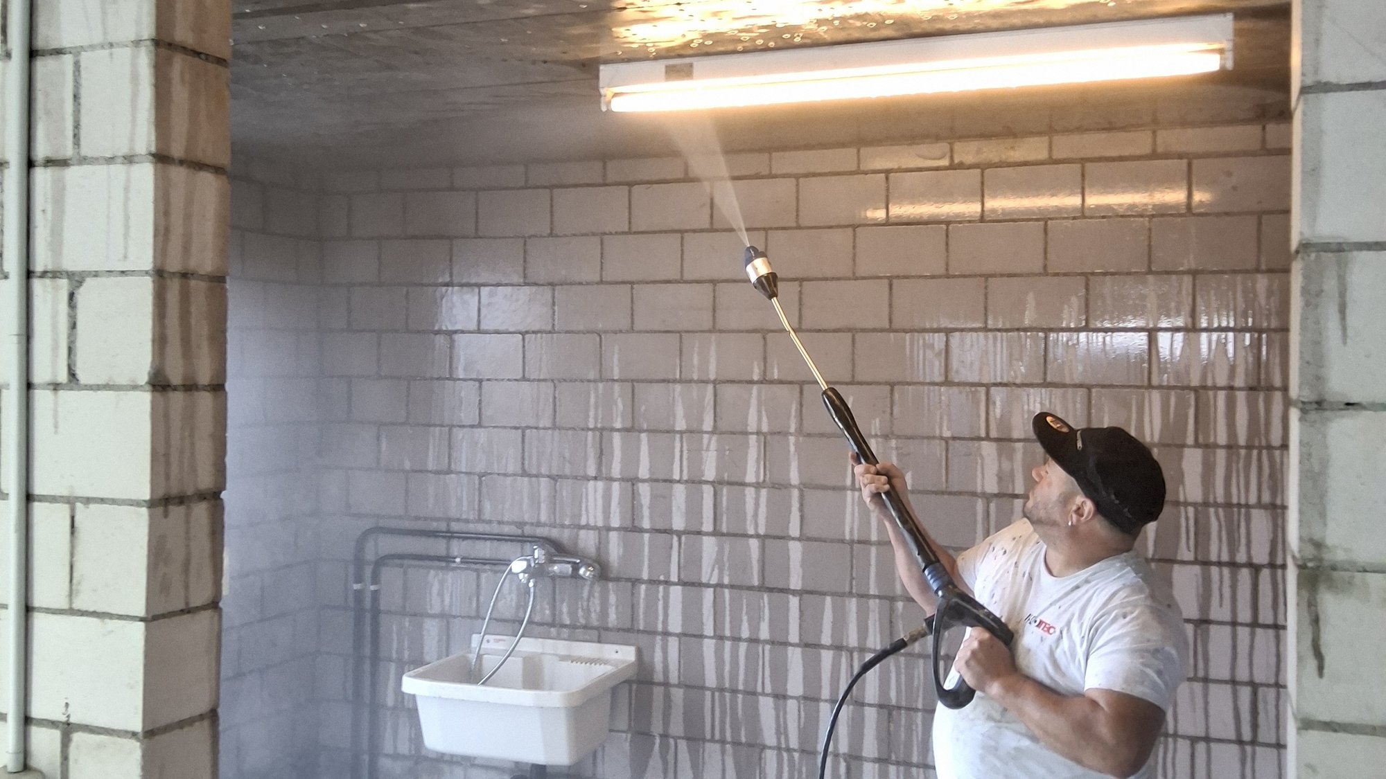 ISOTEC Mitarbeiter spritzt transparente Flüssigkeit auf Fliesenwand in Kellerraum.