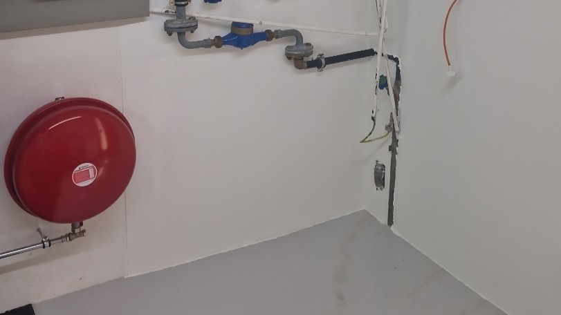 Rotes Ausdehnungsgefäß und blauer Wasserzähler an weißer Wand mit Metallrohren