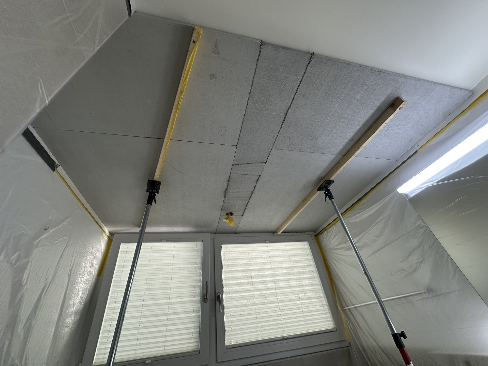 Abgehängte Deckenplatten mit abgeklebten Kanten, abgestützt von Baustützen im Raum.