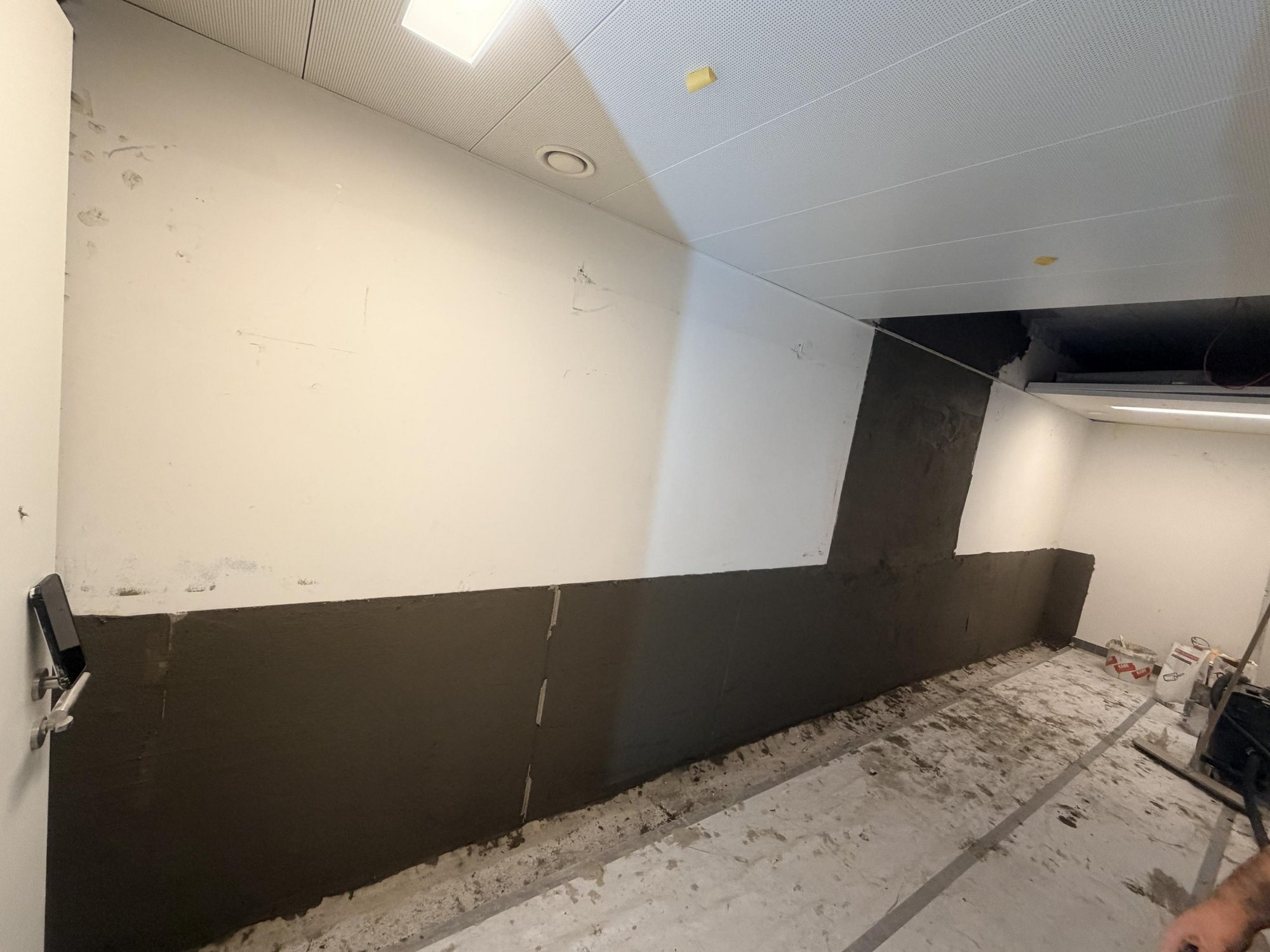 Schwarze Plattenverkleidung entlang einer Wand in einem Zimmer, Boden abgedeckt.